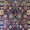 Macro pile detail of a hand-knotted Iranian Khalkhal wool rug showing the intricate curvilinear floral vines in gold, red, and olive green against an intense blue backdrop.