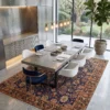 Industrial modern dining area with a poured concrete table and steel-framed chairs, styled over a traditional blue and orange Khalkhal wool rug.