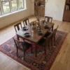 Sophisticated dining room featuring a long wooden table and matching dark chairs, centered over an intricate 7x10 Sabzevar area rug under a brass chandelier.