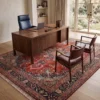 Professional home workspace with a walnut desk and leather chairs, centered over a detailed red and navy Sabzevar Persian wool rug.