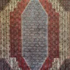 Close-up macro shot of the central medallion on an Iranian Seneh wool rug, showcasing the dense slate blue, red, and cream geometric motifs.