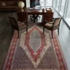 Professional home workspace with a mahogany desk and leather chair, highlighted by a red and navy blue Seneh Persian wool rug in front of high-rise city views.