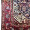 Close-up corner view of a red and navy Persian Tabriz rug highlighting the multi-guard botanical border, cream framing, and neat fringe lines.