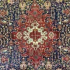 Close-up macro shot of the central diamond medallion on an Iranian Tabriz wool rug, showing the high-density red, navy blue, and cream floral details.