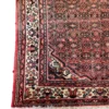 Detailed corner view of a hand-knotted Iranian Hoseinabad rug showing the cream border pattern and fringe edge.