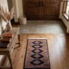Elegant home library hallway with arched doorways and walnut bookshelves, featuring a small navy Pakistan Jaldar runner centered on polished light concrete floors alongside a wooden cane and leather loafers.