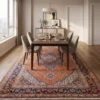 Hand-knotted Persian Mahi rug beneath a modern walnut dining table with beige chairs in a sunlit room.