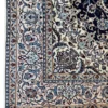 Detailed corner view of a hand-knotted Nain Persian rug showing the ivory floral border and neat fringe edge.