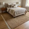 Warm golden-tan Afghan Gabbeh wool rug extending from under a bed with neutral linens in a cozy bedroom suite.