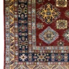 Detailed corner view of an Afghan Kazak wool rug showing the navy geometric border, gold outer guard band, and fringe.