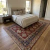 Red and blue Afghanistan Kazak wool rug extending beneath a king bed in a bright, modern bedroom suite.