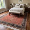 Terracotta Indian Sarough wool rug extending beneath an upholstered bed with a bench in a cozy master bedroom.