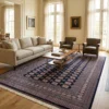 Dark navy Pakistan Bokhara wool rug styled in a spacious, sunlit living room with a cream sofa and coffee table.