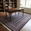 Hand-knotted navy Pakistan Bokhara area rug in a luxury home office under a mahogany writing desk and leather chair.