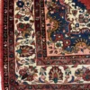 Detailed corner view of a Persian Hamedan wool rug showing navy spandrels, a cream floral border, and short white fringe.