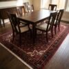 Persian Hoseinabad wool carpet placed beneath a dark wood dining table with six chairs.