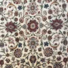 Close-up of the delicate floral vine pattern and fine wool pile on a cream Persian Mashhad area rug.