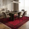 Hand-knotted Afghan Torkman area rug placed under a dark wood dining table with six curved taupe velvet chairs in an elegant dining room.