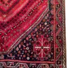 Detailed corner view of a Persian Shiraz wool rug displaying the dark navy spandrel, cruciform tribal crest, and geometric guard bands.
