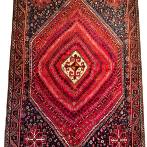 Full overhead view of a 5' 9" x 7' 5" hand-knotted Persian Shiraz wool rug featuring a large stepped red diamond medallion with dense concentric filler patterns, dark navy spandrels, and geometric borders.