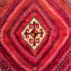 Close-up of the stepped ivory core medallion, concentric tribal bands, and plush hand-knotted wool pile on a red Persian Shiraz rug.