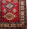 Detailed corner view of an Afghan Kazak wool runner rug showing an ivory rosette border, stepped sunburst medallion, and neat fringe edge.