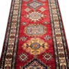 Angled close-up of stepped diamond and octagonal sunburst medallions along the red hand-spun wool pile of an Afghan Kazak runner rug.