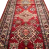 Angled close-up of octagonal rosettes, stepped diamond medallions, and lustrous hand-spun wool pile on an Afghan Kazak runner rug