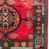 Detailed corner view of an Afghan Uzbek wool rug showing the dark green floral border, red field, and white fringe edge.