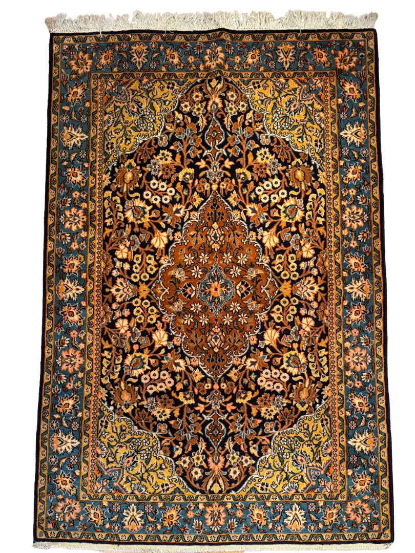Full overhead view of a 4' 3" x 6' 6" hand-knotted Persian Isfahan wool and silk rug with a cognac medallion, midnight blue floral field, and turquoise-blue Shah Abbas border.
