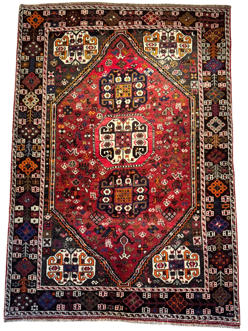 Full overhead view of a 5' 5" x 7' 8" hand-knotted Persian Shiraz wool rug featuring a large hexagonal red field with three stacked tribal medallions and dark espresso geometric spandrels.