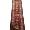 Full overhead view of a 2' 6" x 10' 0" hand-knotted Afghan Kazak wool runner rug featuring a vertical row of geometric tribal medallions in blue, gold, and ivory on a rich crimson red field.