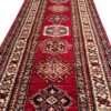 Angled close-up of stepped diamond and octagonal tribal medallions along the red hand-spun wool pile of an Afghan Kazak runner rug.