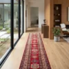 Long Afghan Kazak wool runner rug centered in a bright hallway alongside a floor-to-ceiling glass courtyard wall and wood paneling.