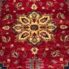 Close-up of the eight-lobed gold medallion, palmette finials, and plush hand-spun wool pile on a crimson Afghan Kazak rug.