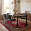 Hand-knotted Afghan Kazak wool rug positioned under a wood dining table and charcoal upholstered chairs beneath a modern chandelier.