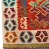 Detailed corner view of an Afghan Kilim wool rug showing the ivory rosette border, flat-woven green selvedge stripe, and fringe.